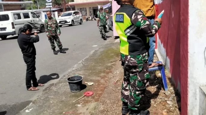 Jaga Kerapian, Babinsa Bersama Warga Cat Pagar Kantor Desa