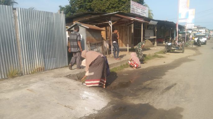 Babinsa Dan Warga Bersihkan Rumput Liar Di Bahu Jalan Dalam Aksi Gotong Royong